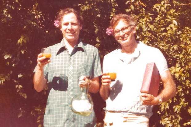 Amos Tversky and Daniel Kahneman smiling and raising glasses in a sunny garden
