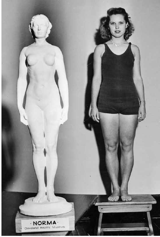 Martha Skidmore in a swimsuit, standing on a stool beside the white Norma statue